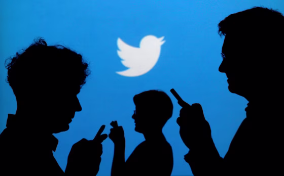 Image: People holding mobile phones are silhouetted against a backdrop projected with the Twitter logo