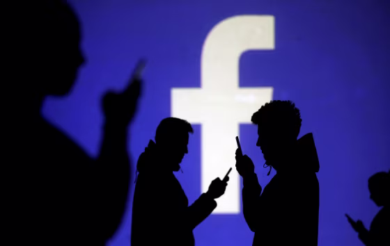 Image: People on phones next to a Facebook logo projection on March 28.