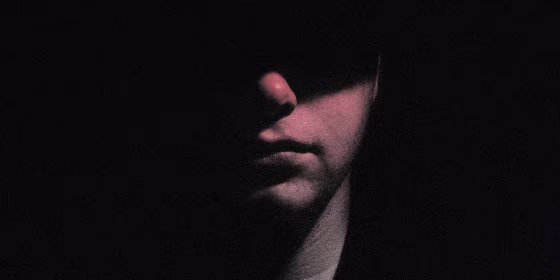 Image: Portrait of a man with half of his face hidden in shadow.