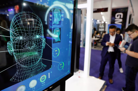 Image: Visitors check their phones behind the screen advertising facial recognition software during Global Mobile Internet Conference (GMIC) at the National Convention in Beijing
