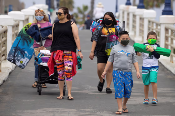Image: People wear face masks as they arrive at the beach in Oceanside, California