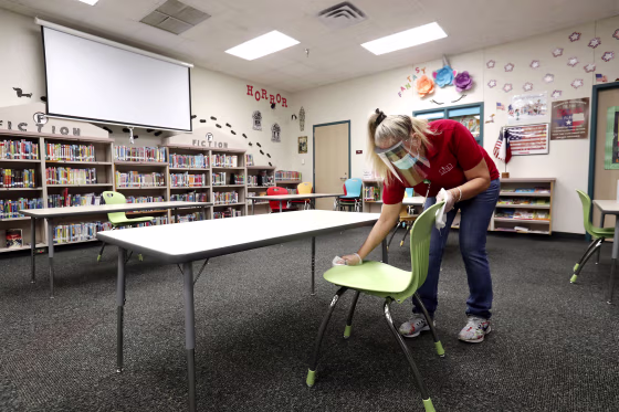 Wearing a mask and a face guard to protect against the coronavirus, custodian Maria Concha wipes down a chair in the library at Stephens Elementary School in Rowlett, Texas, on Wednesday.
