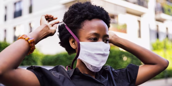 Woman putting on face mask. Shop popular face masks meeting CDC requirements from Adidas, Reebok, Athleta, Anthropologie, Etsy, Casetify, Buck Mason and more.