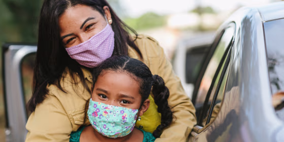 A woman and a girl outdoors wearing colorful and patterned cloth face masks.