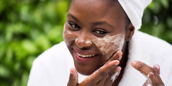 Woman in bathrobe and towel washing away face makeup with cleansing oil
