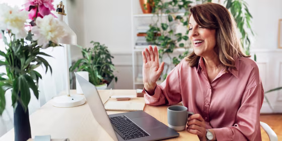 Woman working from home wearing silk pink top video calling on laptop