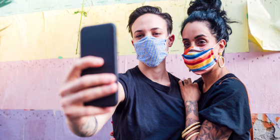 couple wearing colorful face masks taking selfie with smartphone