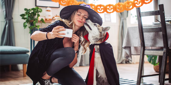 Woman and dog dressed in halloween costumes taking selfie at home