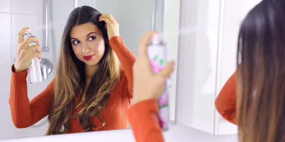 woman spraying dry shampoo in hair in mirror