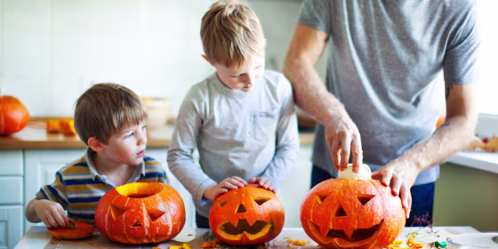 father and sons carving halloween pumpkins in kitchen