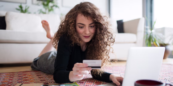A young teenage girl with laptop, camera and map holding a card, making online payment.