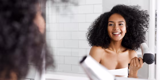 Woman blow drying her hair in a bathroom with a small blow dryer