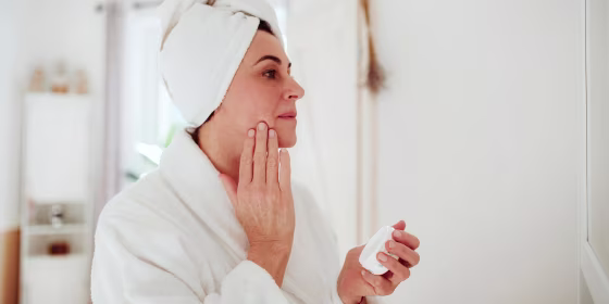 Woman rubbing lotion on her face in a bathrobe, from Dermstore