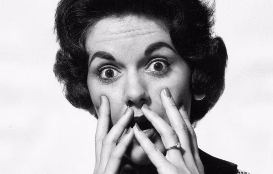 Image: A woman with a scared expression holds her hands up to her face