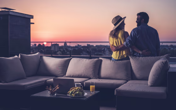 Rear view of happy couple communicating on a penthouse balcony at sunrise.