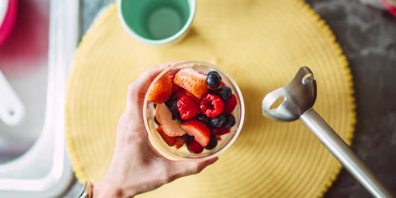 Overhead view of a cup of fruit and an immersion blender