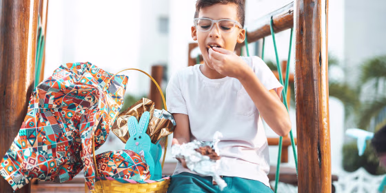 Little boy with glasses, eating chocolate out of a packaged Easter Basket