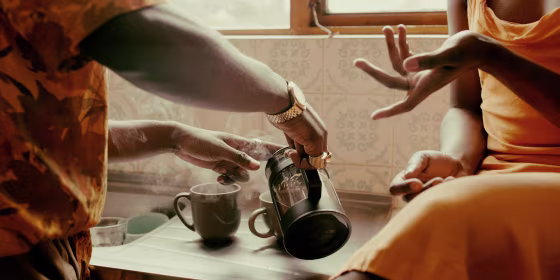 Close up image of a man and woman in a kitchen, pouring two cups of steaming coffee, from a French Press