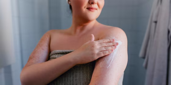Woman in a towel, in her bathroom, rubbing lotion on her arm