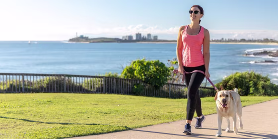 Woman wearing black leggings and a pink tank, walking her dog outside