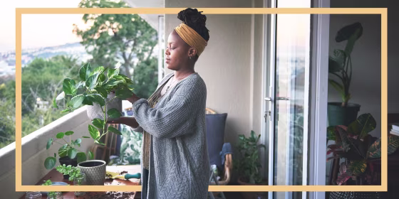 Woman gardening on her balcony wearing a grey cardigan and yellow headband