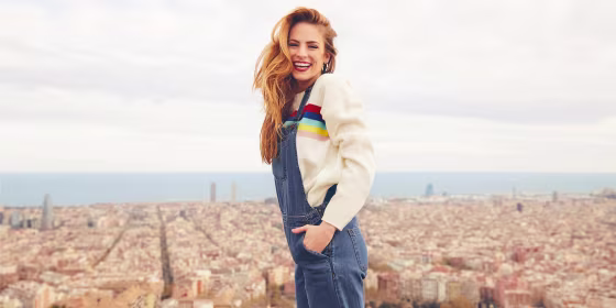 Red-head Woman wearing jean overalls with a beige sweater, outside