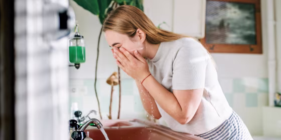 Woman washing her face, leaning over her sink, in the bathroom