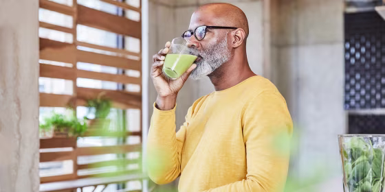 Man leaning on a counter drinking green juice