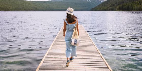 Young woman walking on dock at mountain lake wearing a jumpsuit