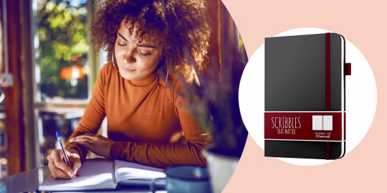 Illustration of a Woman writing in her journal at a desk and the A5 Dotted Journal by Scribbles That Matter  in black. See the best bullet journal notebooks and planners of 2021. Learn how to bullet journal and how it can help organize your life and impro