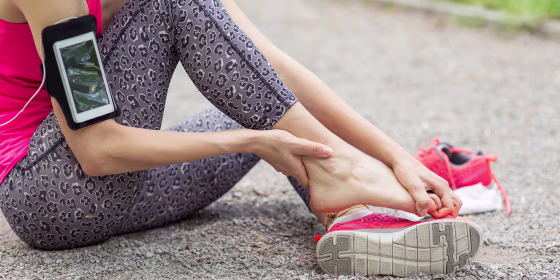 Woman sitting on the ground rubbing her foot out of her pink sneaker