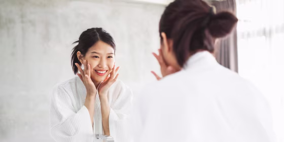 Woman Looking At Her Face On Mirror In Bathroom