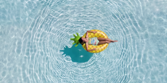 An aerial view of teenage girl relaxing in the swimming pool on a pineapple floatie
