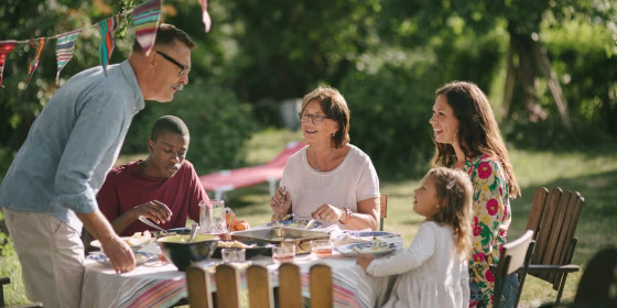 Senior man and granddaughter talking while having lunch with family in backyard during party