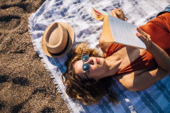 Woman lies on the beach reading a book