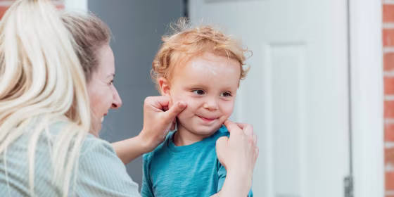 Woman putting sun cream on her son's face while he is looking away from her and the camera, outdoors in their home garden
