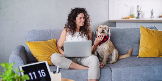 Woman with pet dog sitting and working indoors at home, using laptop