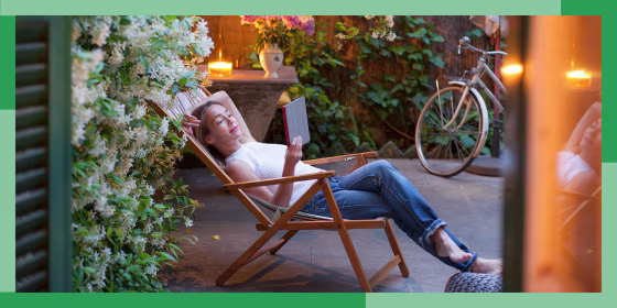 Woman relaxing on deck chair in backyard at dusk, reading on digital tablet