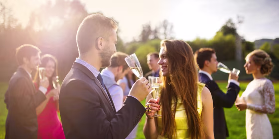 Wedding guests clinking glasses while the newlyweds drinking champagne in the background