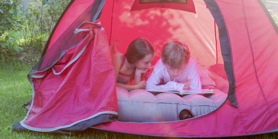 Boy and girl reading lying in a red tent with a book