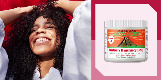 Close-up of young woman against red wall with curly hair and a bottle of Aztec Healing clay