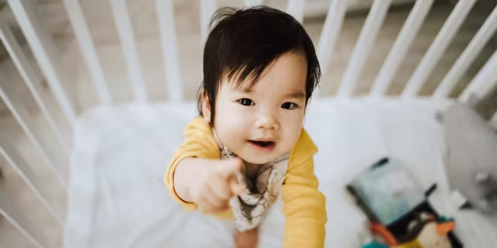 Adorable baby girl standing in her crib and pointing away with fingers