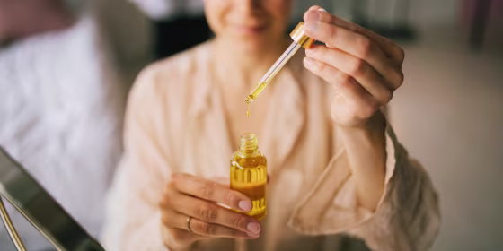 Image of Woman holding natural face oil in her bedroom