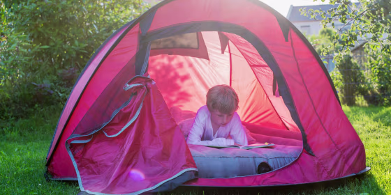 Boy reading in a red tent at evening twilight on an air mattress