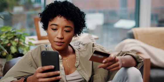 Shot of a young woman holding her credit card while using her cellphone at home