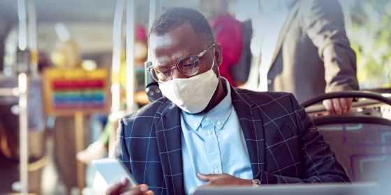 usinessman using a phone while commuting on a bus, wearing a mask and glasses