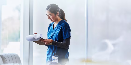 Smiling female nurse examining document in hospital lobby