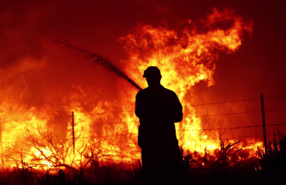 A utility worker uses a hose to extinguish fire near power poles as the Dixie Fire moves through the area on Aug. 16, 2021, near Janesville, Calif.