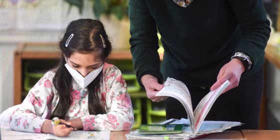 A teacher browses a book next to a second-grade pupil wearing a face mask during lessons at the Petri primary school in Dortmund, western Germany, on February 22, 2021, amid the novel coronavirus COVID-19 pandemic