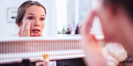 Woman applying makeup in front of a big mirror.